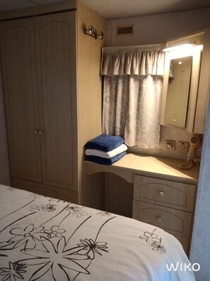 Un dormitorio con cama, cómoda, espejo y una pila de toallas.