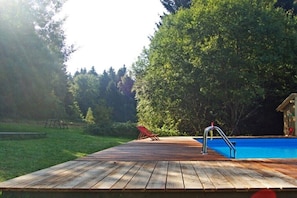 Eine Holzterrasse mit Pool, umgeben von Bäumen.