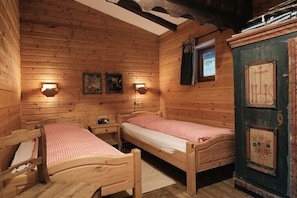 Ein Zimmer in einer Holzhütte mit zwei Betten aus Holz, einem Nachttisch, einer Wandleuchte und einer Tür mit dekorativer Verkleidung.