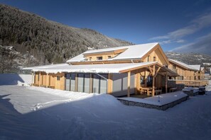 A wooden lodge with a sloped roof, a covered patio, and a view of a snowy mountain. - Cabin in Murau with swimming pool (Murau)