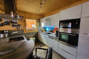 A modern kitchen with stainless steel appliances, a wooden ceiling, and a window with a view of the outdoors. - Cabin in Murau with swimming pool (Murau)