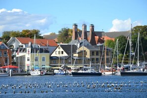 Ein Hafen mit Booten, ein Gebäude mit Schornsteinen und eine Reihe von Häusern.