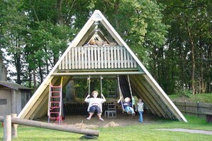 Eine dreieckige Holz-Spielkonstruktion mit Schaukeln und einer Kletterleiter.