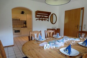 Ein Essbereich mit einem runden Holztisch, gedeckt für vier Personen, mit einer Küche im Hintergrund und einer Holztür.