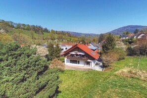 Una casa con techo rojo, rodeada de vegetación y colinas al fondo.