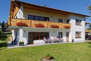 Ein zweistöckiges Haus mit Balkon, einer Terrasse mit Sitzgelegenheiten und einem gepflegten Rasen.