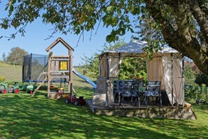 Ein Spielplatz mit Rutsche, Klettergerüst und einem Zeltähnlichen Unterstand mit Stühlen.