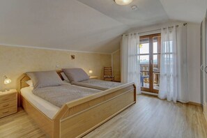 Ein Schlafzimmer mit einem hölzernen Bett, Nachttischen, einem Sessel und einem Fenster mit Vorhängen.