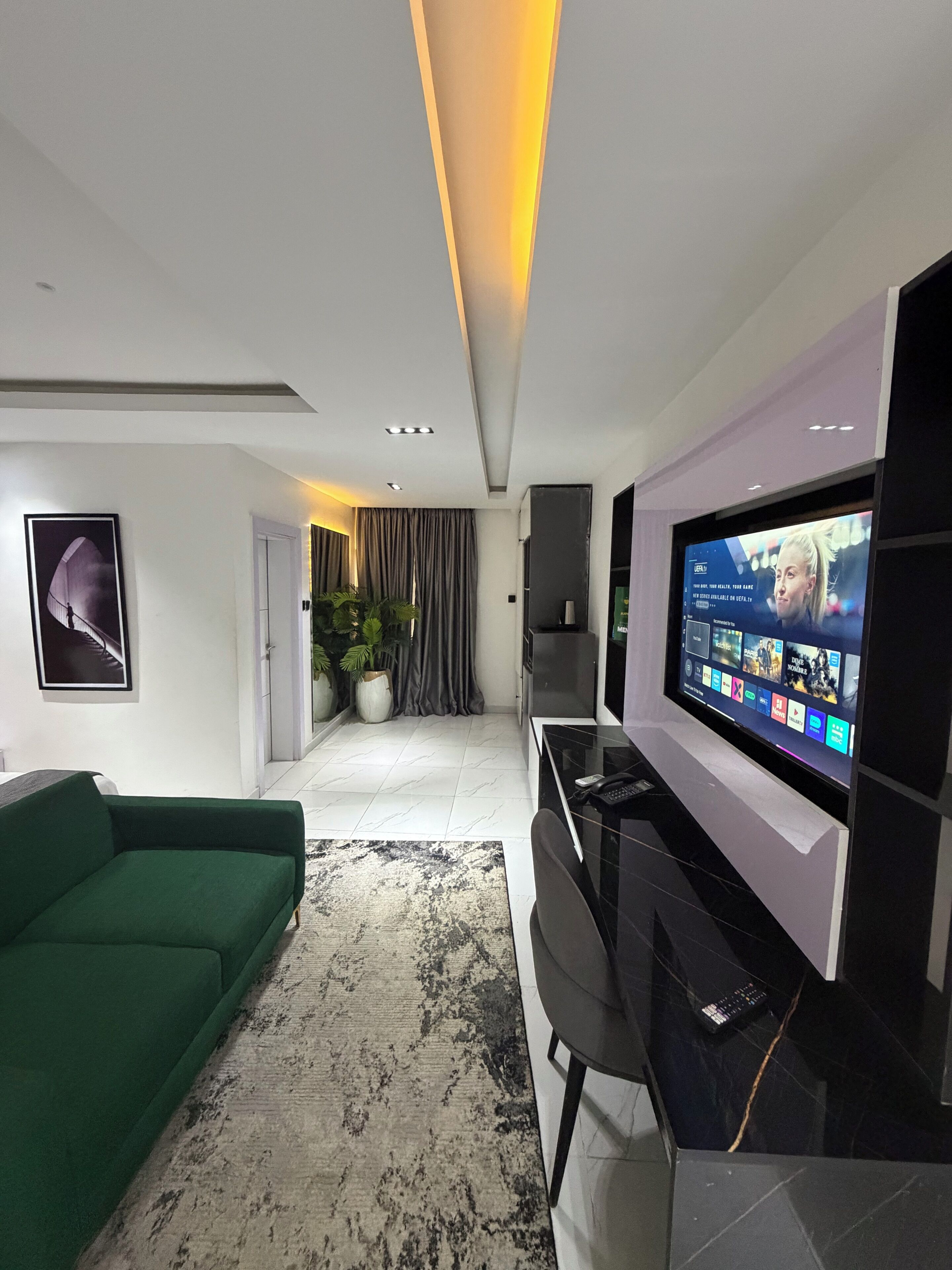 A modern living room with a green sofa, a large flat-screen TV, and a minimalist design.