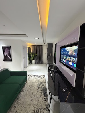 A modern living room with a green sofa, a large flat-screen TV, and a minimalist design.