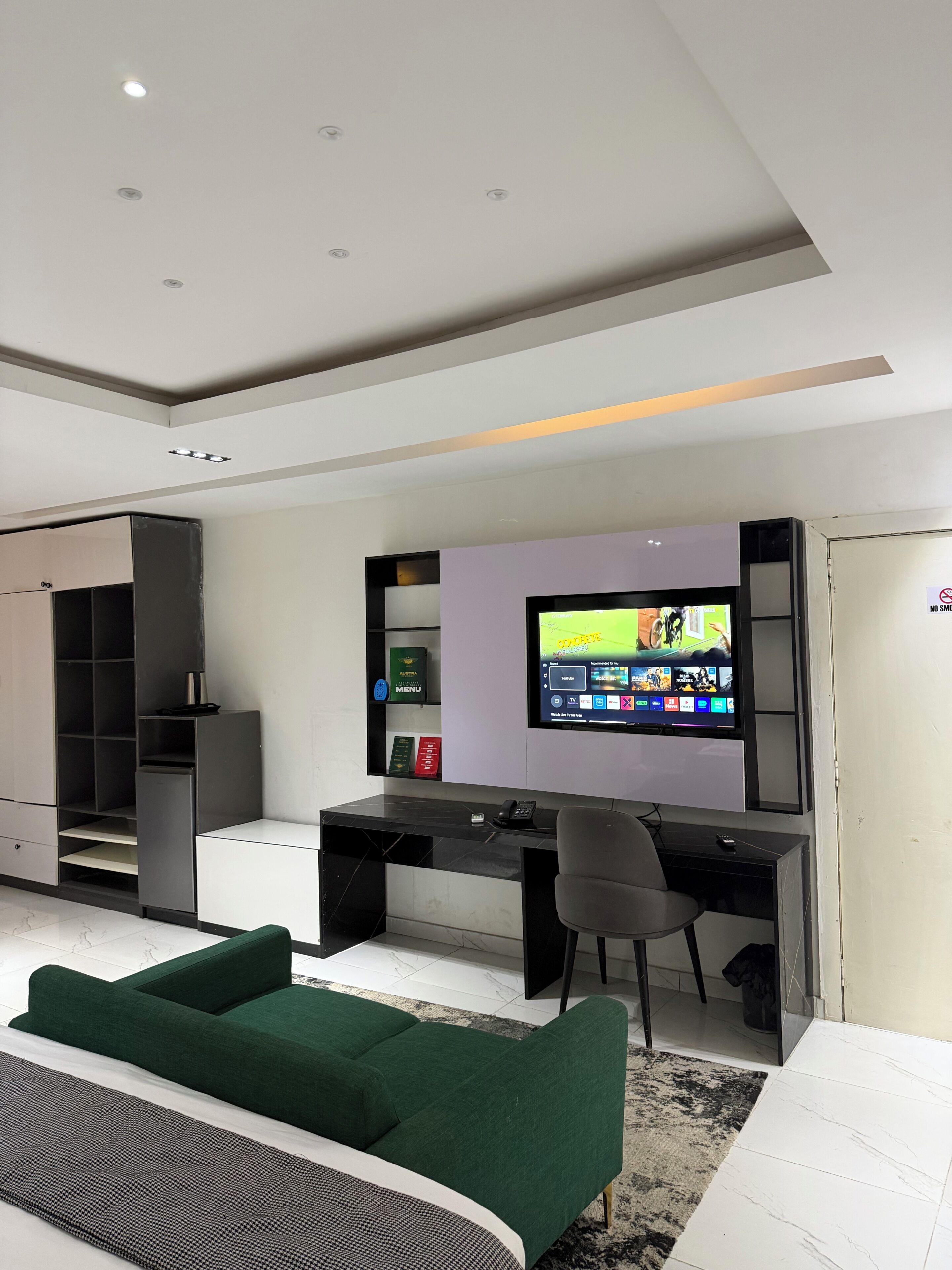 Een moderne woonkamer met een flatscreen televisie, een bureau, een groene bank en een inbouwkast.