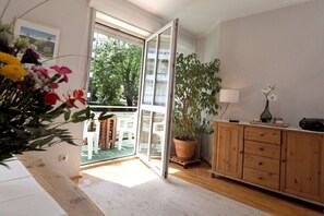 Ein Zimmer mit einer Schiebetür zum Balkon, einem Holzschrank, einer Topfpflanze und einem kleinen Tisch mit Lampe.