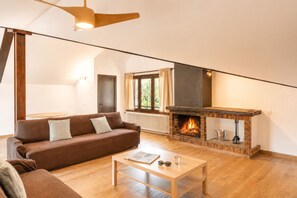 Ein Wohnzimmer mit einem braunen Sofa, einem Holztisch, einem Kamin und einem Deckenventilator.