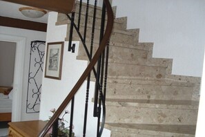 A spiral staircase with a wooden handrail and black metal balusters, leading to a landing with a white door and a decorative metal piece. - Holiday apartment with 2 bedrooms (Steinberg)