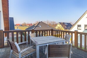 Eine Holzterrasse mit Tisch und Stühlen, Blick auf Häuser und einen klaren Himmel.