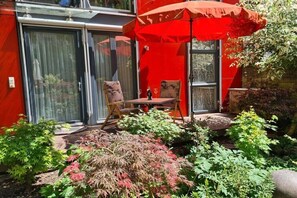 Un patio con una sombrilla roja, una mesa y sillas.