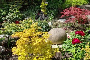 Un jardin avec différentes plantes, une sculpture en pierre et une fleur rouge.