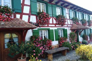 Ein traditionelles Fachwerkhäuschen mit grünen Fensterläden, Blumenkästen und einem Kopfsteinpflasterhof.