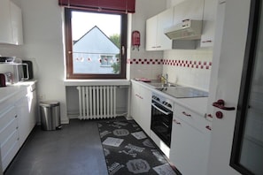 A compact kitchen with white cabinets, a window, a radiator, a sink, and an oven. - Holiday apartment in Essen with swimming pool (Essen)