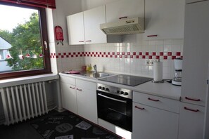 Eine Küche mit weißen Schränken, einem Herd, einem Backofen, einer Spüle und einem Fenster mit Blick auf Bäume.