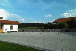 Ein gepflasterter Innenhof mit einer Steinmauer, ein kleines weißes Gebäude mit roten Ziegeln und einem bewaldeten Hintergrund.