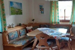 Ein gemütliches Zimmer mit einer hölzernen Bank, einem Tisch mit einer blumigen Tischdecke und einem Fenster mit Vorhängen.