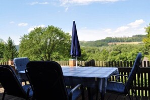 Eine Terrasse im Freien mit Tisch und Stühlen, einem Holzzaun und Blick auf eine grüne Landschaft.