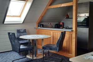 A loft-style room with a skylight, a round table with chairs, a kitchenette with a stove and oven, and wooden paneling. - Holiday apartment with 1 bedroom (Prerow\/Ostseebad)