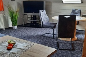 A modern room with a flat-screen TV, grey upholstered chairs, a round table, and a potted plant. - Holiday apartment with 1 bedroom (Prerow\/Ostseebad)