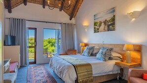 A bedroom with a large bed, a TV, a wooden nightstand, a lamp, a painting, and a balcony with a view. - Cycads On Sea (Saint Francis Bay)