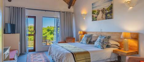 Un dormitorio con una cama grande, un televisor, una mesita de noche de madera, una lámpara, un cuadro y un balcón con vistas.