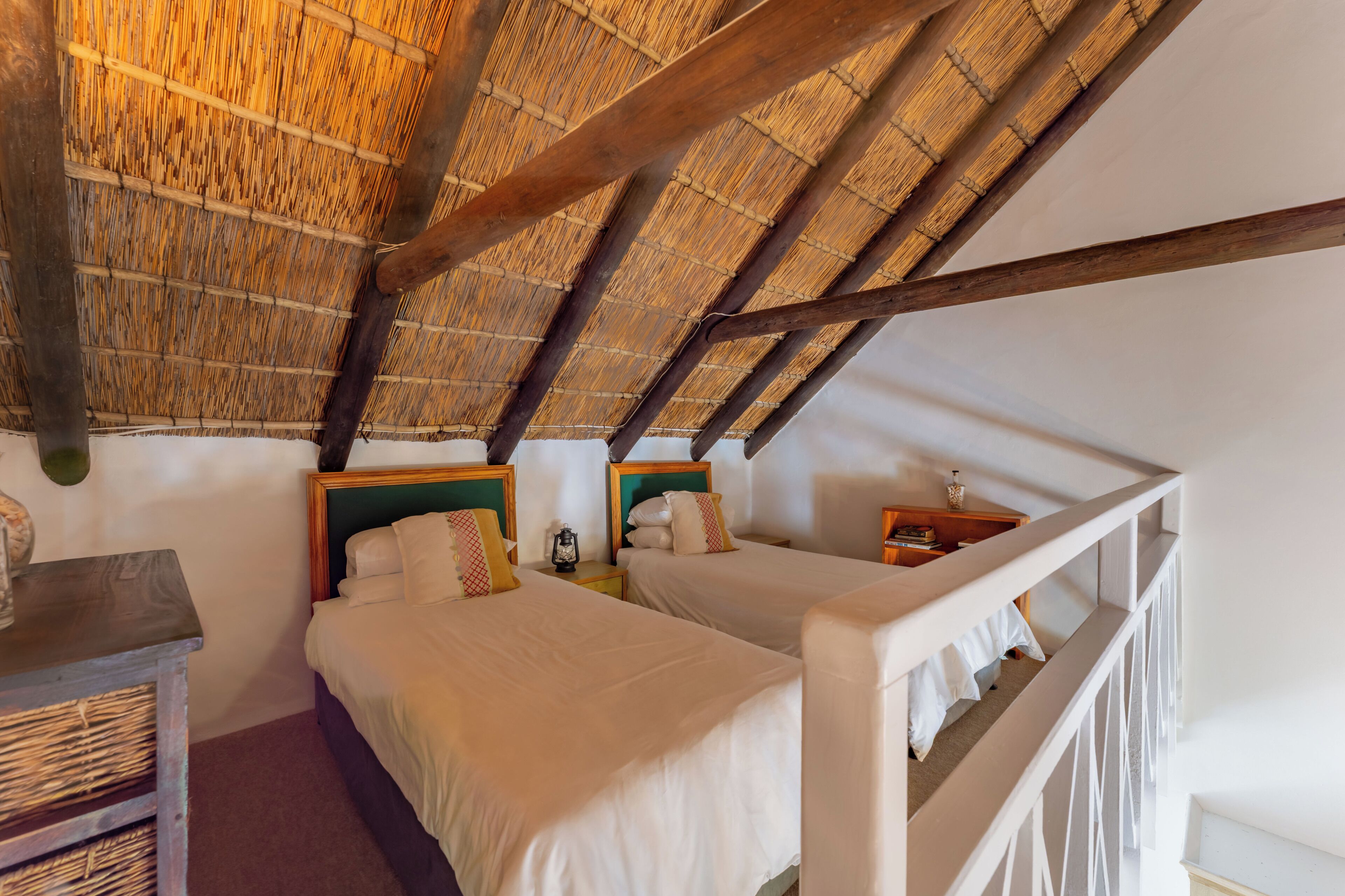 A room with two beds, a wooden ceiling, and a white railing.