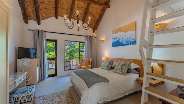 A bedroom with a bed, a TV, a fan, a chair, a desk, a staircase, and a balcony with a view of greenery. - Cycads On Sea (Saint Francis Bay)