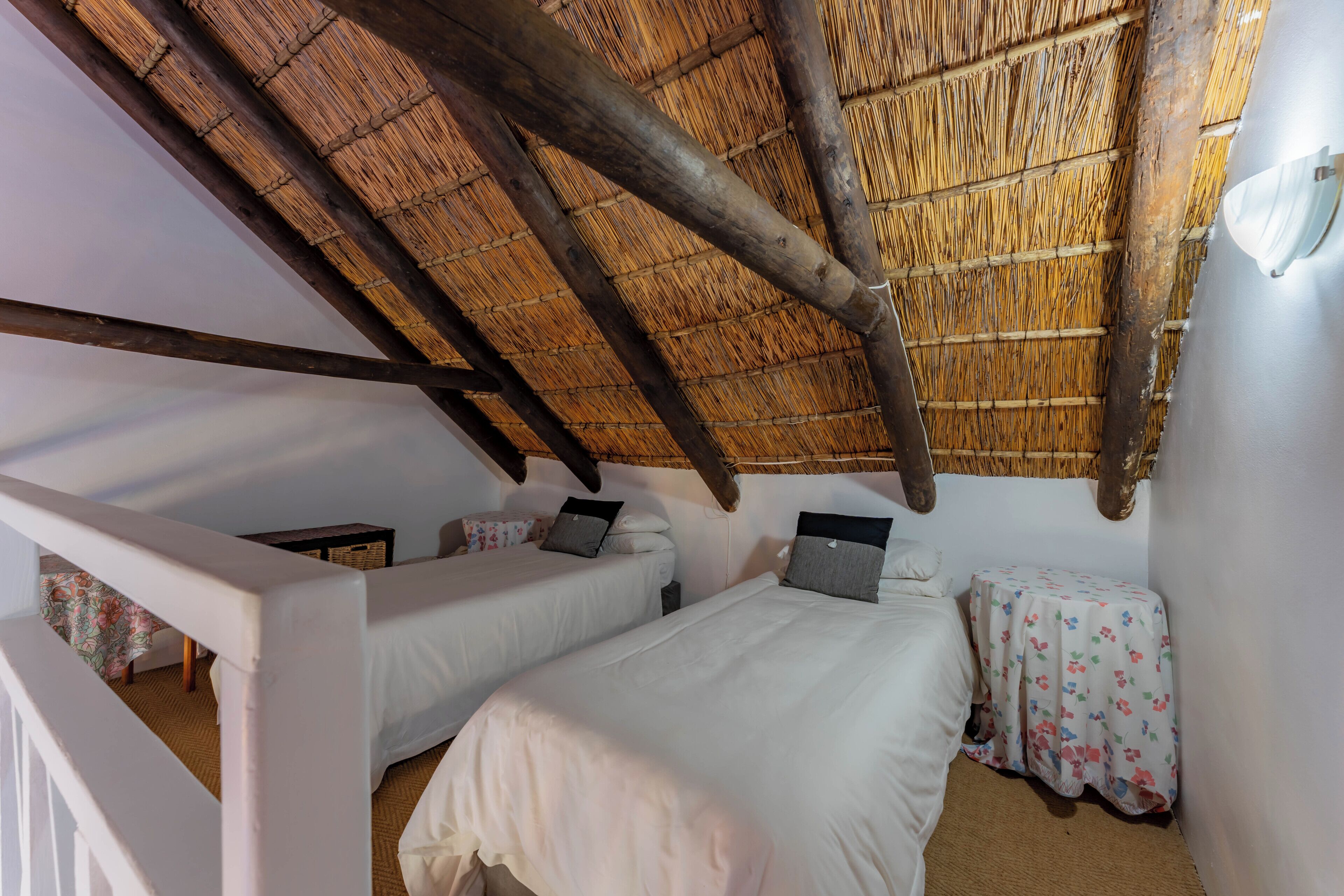 A room with two beds, a small table, and a thatched roof.
