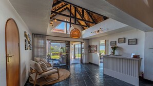 A spacious room with a high ceiling, a reception desk, a seating area with a woven chair, and a view through large glass doors. - Cycads On Sea (Saint Francis Bay)