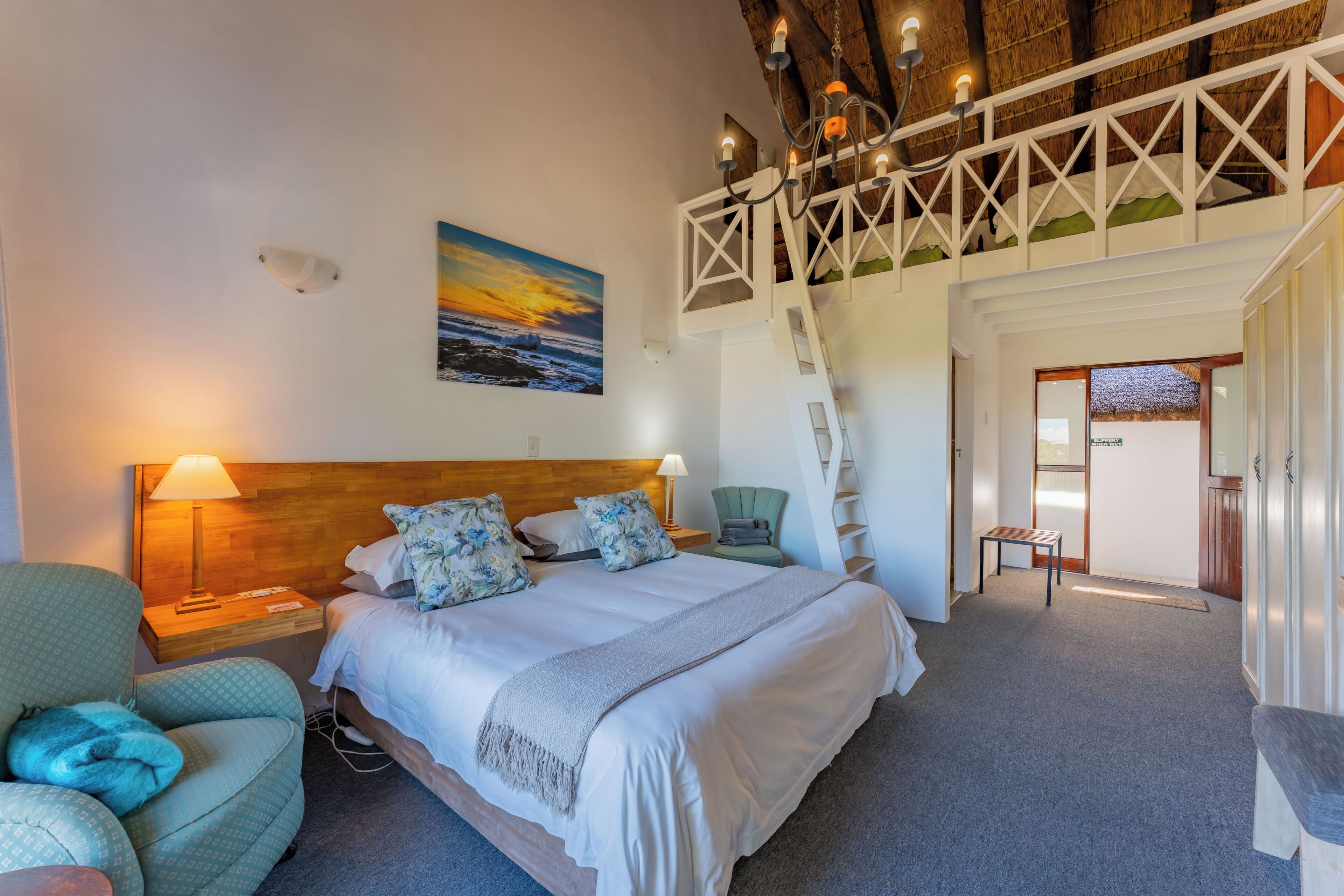 Une chambre à coucher comprenant un lit, une table de chevet, une chaise, un bureau et un escalier menant à un niveau supérieur.