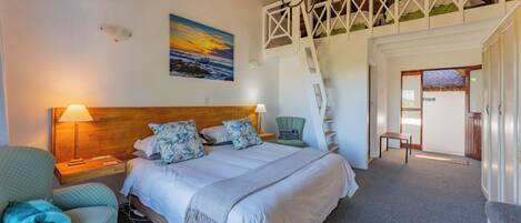 A bedroom with a bed, a nightstand, a chair, a desk, and a staircase leading to an upper level.