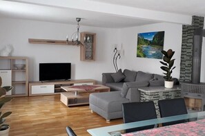 Una sala moderna con televisor de pantalla plana, sofá gris, mesa de centro de madera y un comedor con mesa de vidrio.