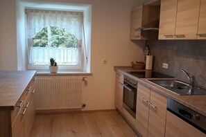 Eine kleine Küche mit Fenster, Holzschränken, integriertem Backofen und Spüle.