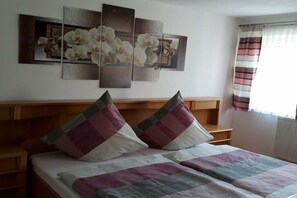 Ein Schlafzimmer mit einem Bett, Kissen, einem Kopfteil, einem Wandbild und einem Fenster mit Vorhängen.