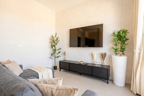 A modern living room with a flat-screen TV, a dark-colored console table, a grey sofa, and two potted plants. - Terrace Penthouse Gargasole SX – Elegant 7th-Floor Retreat with Terrace in Bari (Bari)