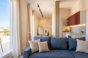 A modern living room with a sofa, a dining table with a mirror, and a kitchen area with cabinets. - Penthouse with Terrace in Gargasole SX – Elegant 7th-Floor Retreat with Terrace in Bari (Bari)