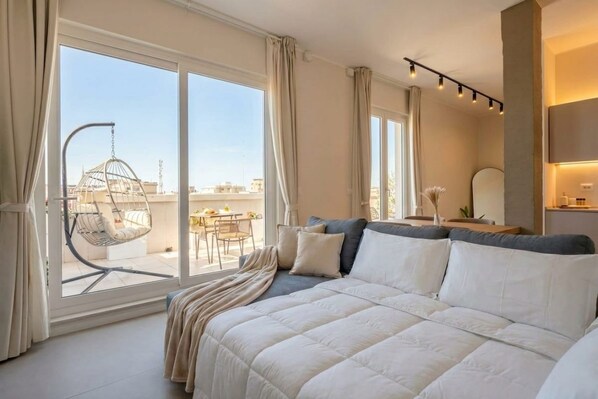 A bedroom with a large bed, a hanging chair, and a view of the cityscape through large windows. - Terrace Penthouse Gargasole SX – Elegant 7th-Floor Retreat with Terrace in Bari (Bari)