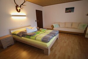 Ein Schlafzimmer mit einem Bett, einem Nachttisch, Holzboden, einer Couch und einer wandmontierten Lampe.