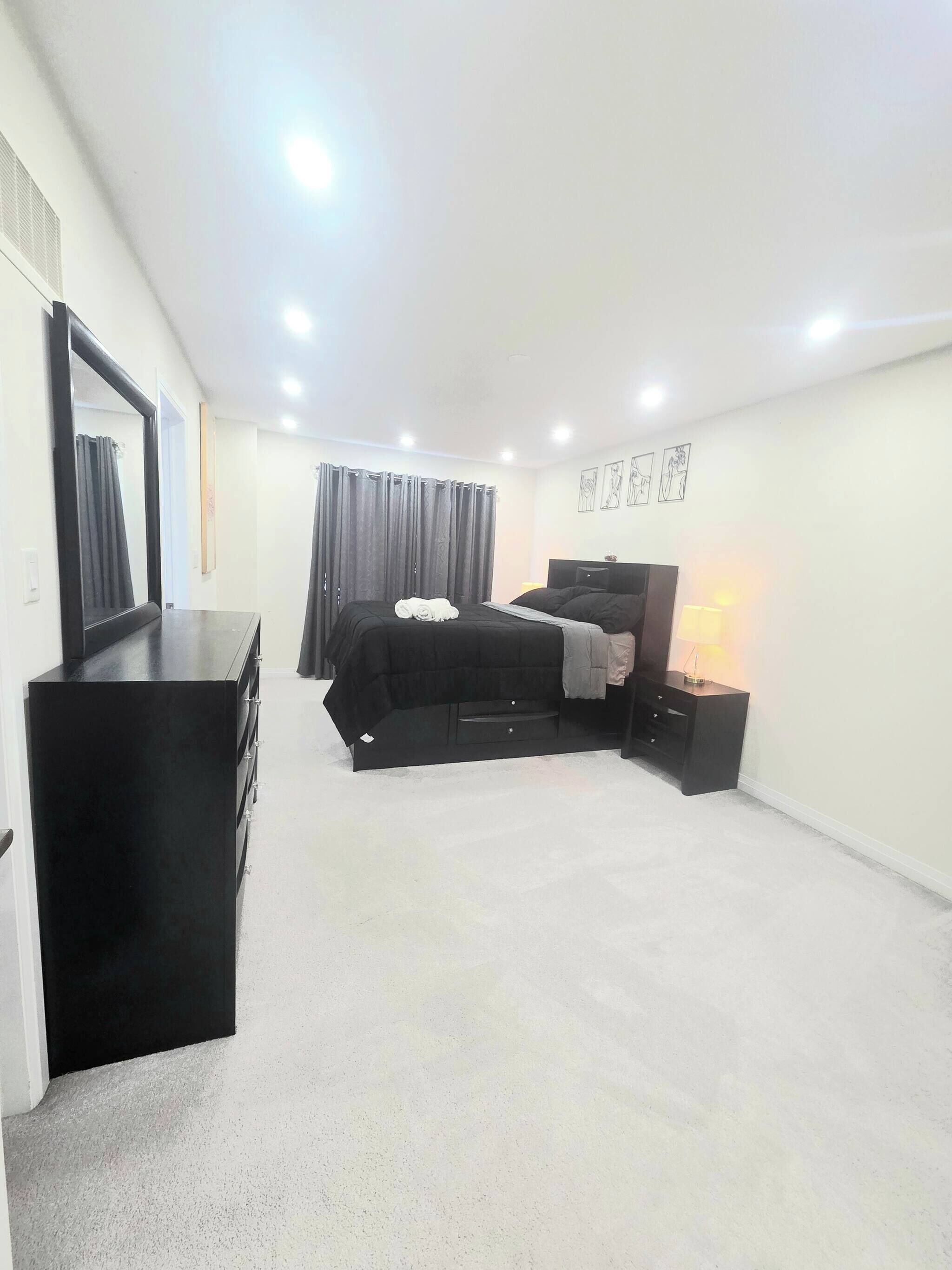 A bedroom with a bed, a dresser, a bedside table with a lamp, and a wall-mounted mirror.