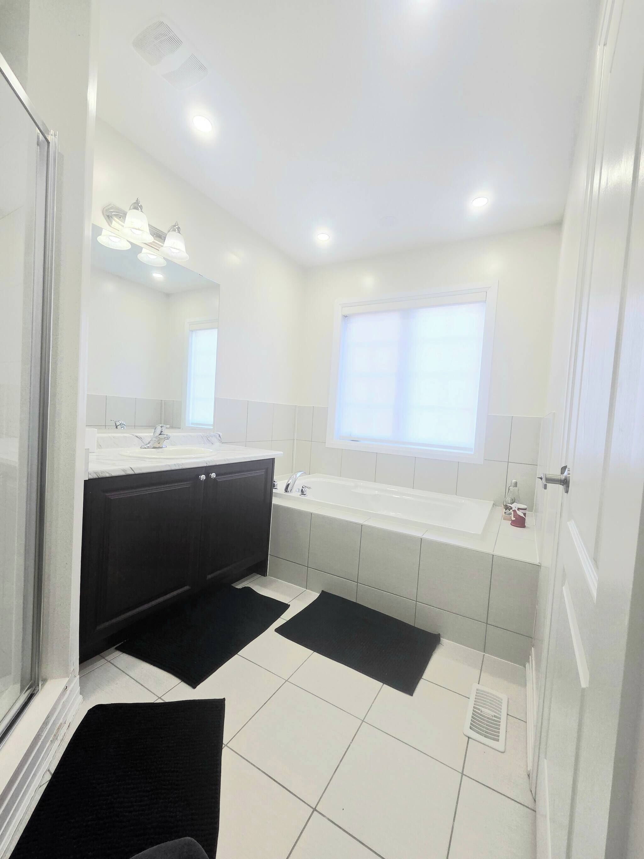 A modern bathroom with a large mirror, a double sink, and a bathtub.