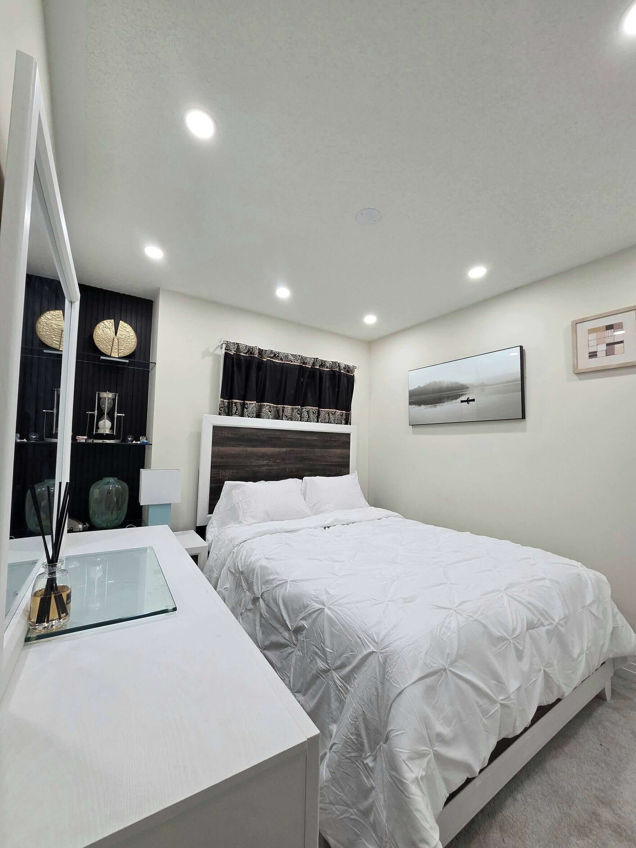 A bedroom with a bed, bedside table, mirror, and a painting on the wall.