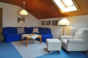 Ein gemütliches Wohnzimmer mit einem blauen Sofa, einem weißen Sessel, einem Holztisch und einer Lampe.