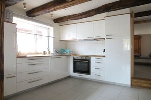 A kitchen with white cabinets, a built-in oven, and a window with blinds. - Holiday apartment with 1 bedroom (Lenningen)