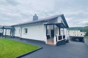 Ein modernes, zweistöckiges Haus mit einer überdachten Veranda, einer gut sichtbaren Hausnummer '10' an der Fassade und einem gepflasterten Auffahrt.
